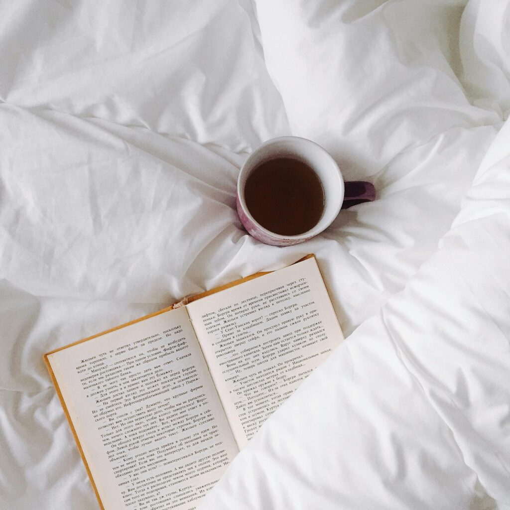 An inviting setup with a warm cup of tea and open book on white bedding, ideal for relaxation.