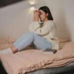 Woman in a cozy bedroom, wearing comfort clothes, meditating with eyes closed.