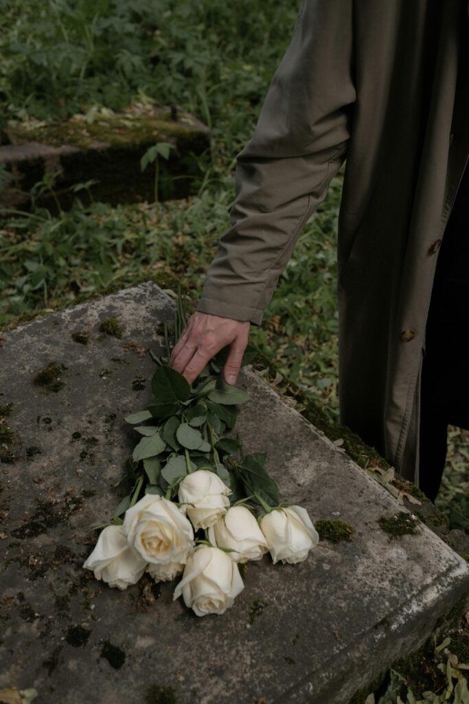 A solemn moment captured as a hand places white roses on a moss-covered tombstone, symbolizing loss and bereavement.